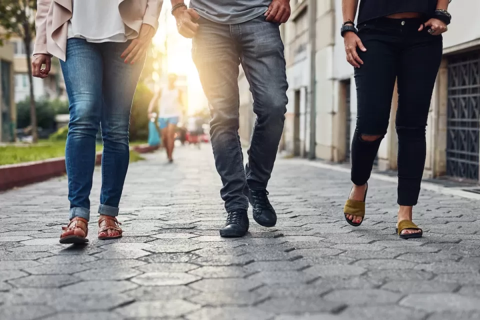 Close-up of bottom half of three people walking down city sidewalk paved with paving stones.